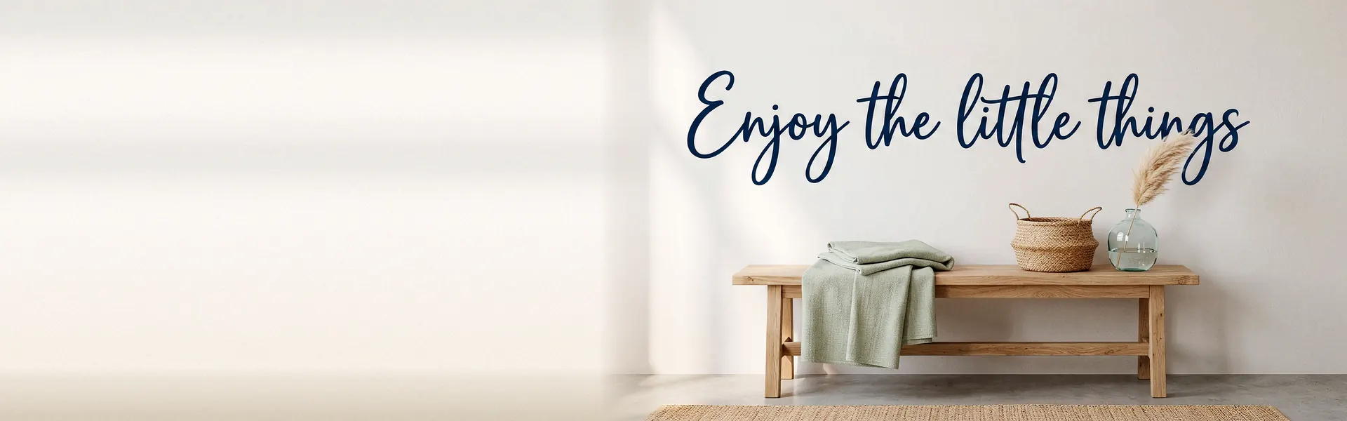 Schriftzug „Enjoy the little things“ als dunkelblaues Wandtattoo über einer Holzbank